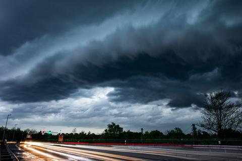 Eine Gewitterfront zieht über eine Landstraße, auf der Autos vorbeifahren.  Symbolfoto: dpa