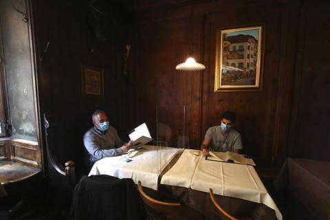 Gäste eines Restaurants in Bozen sitzen mit Mundschutz am Tisch und sind durch eine Plexiglasscheibe voneinander getrennt. Foto: dpa